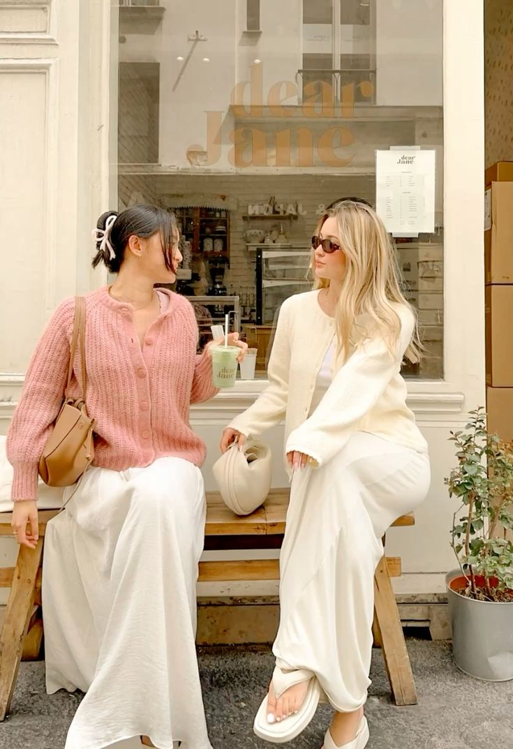Two women in stylish outfits sitting outside a store with 'dear lune' sign.